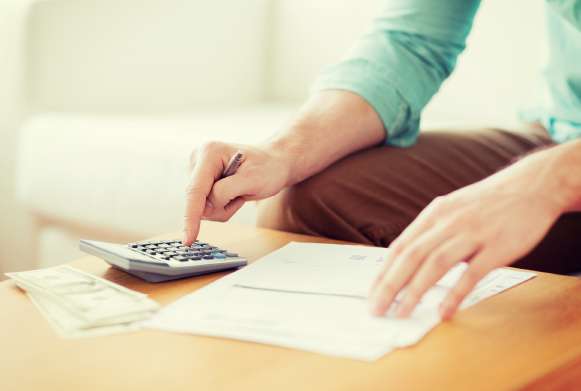 Imagem mostra uma pessoa teclando em uma calculadora e papéis sobre a mesa