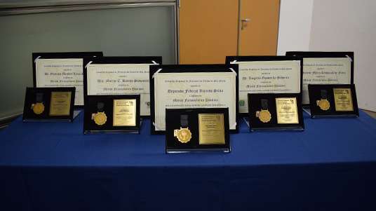 Cinco medalhas e placas comemorativas em cima de uma mesa azul 